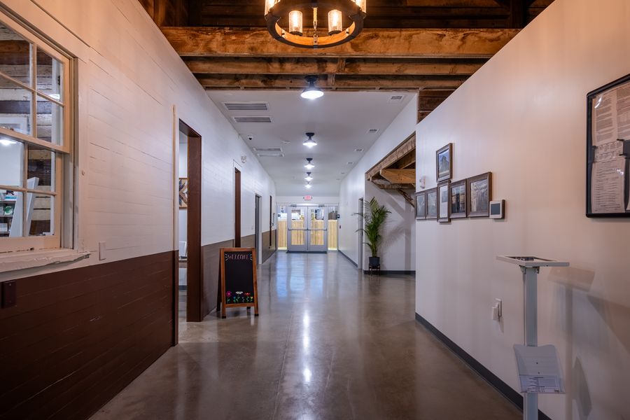A restored hallway with original painted board walls, exposed beams overhead, a chalkboard welcome sign and framed restoration photographs.