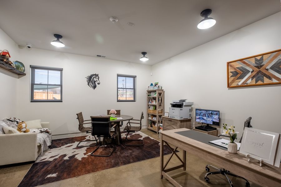 The front office with a wooden desk, a round meeting table and chairs, a cowhide rug, a bookshelf of family resources and a guest book by the door.