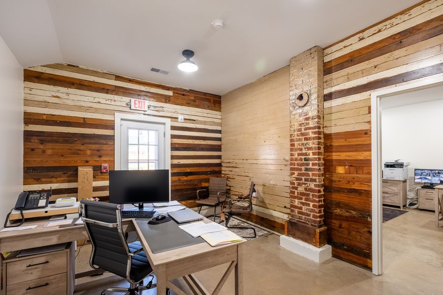 An administrative office lined with reclaimed barn boards in mixed browns and creams, an exposed brick chimney, and a desk with a monitor and phone.